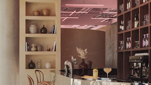 A modern bar area with wooden chairs, a counter with a coffee machine, shelves with bottles, and a vase with dried flowers. - OKKO Hotels Paris la Défense (Nanterre)