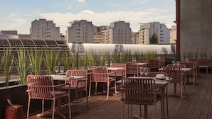 A rooftop terrace with wooden flooring, wicker chairs, and tables set for dining. - OKKO Hotels Paris la Défense (Nanterre)