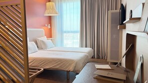 A hotel room with two beds, a desk, a TV, and a window with curtains.