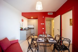 A dining area with a table set for four, a red sofa, and a kitchen in the background.
