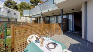 Un espacio exterior moderno con comedor, una mesa dispuesta para dos personas, cerca de una valla de madera y un edificio con balcón.