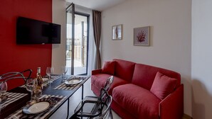 Una sala de estar moderna con un sofá rojo, una mesa de comedor para dos personas y un televisor montado en la pared.