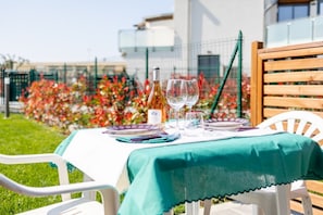 A table set outdoors with a white tablecloth, wine bottle, glasses, and plates.