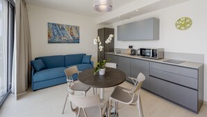 Ein modernes Wohnzimmer mit einem blauen Sofa, einem Esstisch mit Stühlen, einer Küchenzeile und einem großen Fenster.