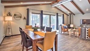 A spacious dining area with a wooden table and chairs, a small side table with a lamp, and a decorative wall with a 'gather' sign. - Modern Lead Cabin w/ Private Hot Tub & Fireplace! (Lead)