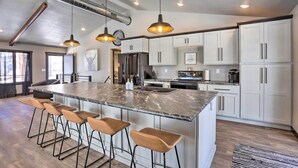 A modern kitchen with a large island, bar stools, white cabinets, and pendant lighting. - Modern Lead Cabin w/ Private Hot Tub & Fireplace! (Lead)