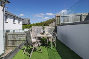 A patio area with a table and chairs, surrounded by a wooden fence and a white wall.