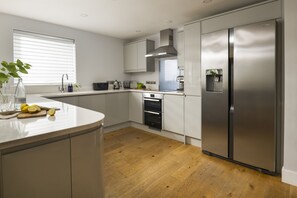 A modern kitchen with a stainless steel refrigerator, built-in oven, and a curved island with a cutting board and lemons. - The Retreat - sleeps 8 guests  in 4 bedrooms (Widemouth Bay)