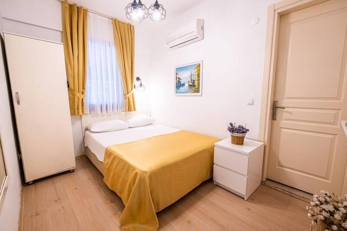 A bedroom with a bed, a bedside table with a lamp, a picture on the wall, and a door.