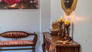 Un banco de madera con un cojín estampado, una mesita de madera con libros y velas, y un espejo en la pared.