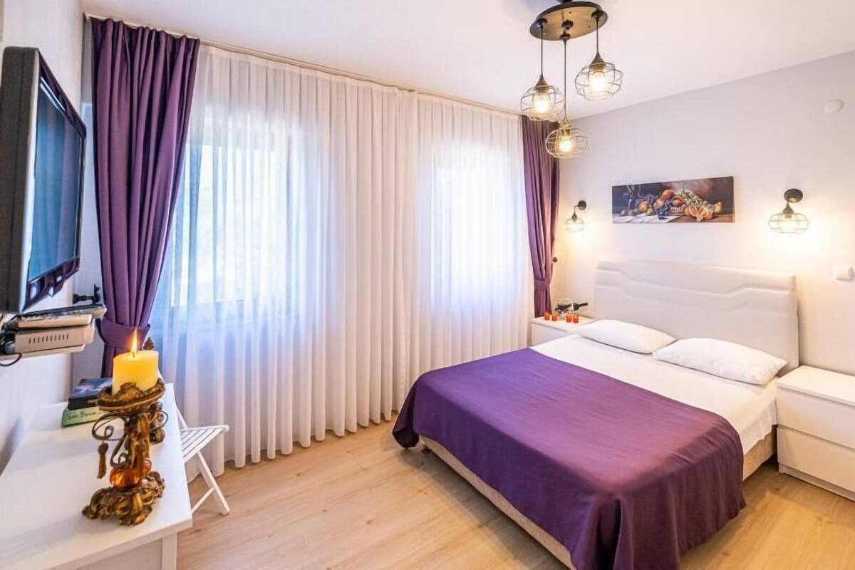 A bedroom with a bed, a nightstand, a TV, and a desk with a lamp.
