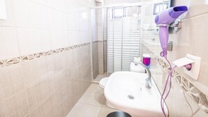 Un baño con lavamanos blanco, cabina de ducha de vidrio y un secador de pelo púrpura en la pared.