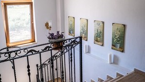 Una escalera con barandilla de hierro forjado negro, una ventana que da a vistas de árboles y una pared con cuatro cuadros de motivos botánicos.