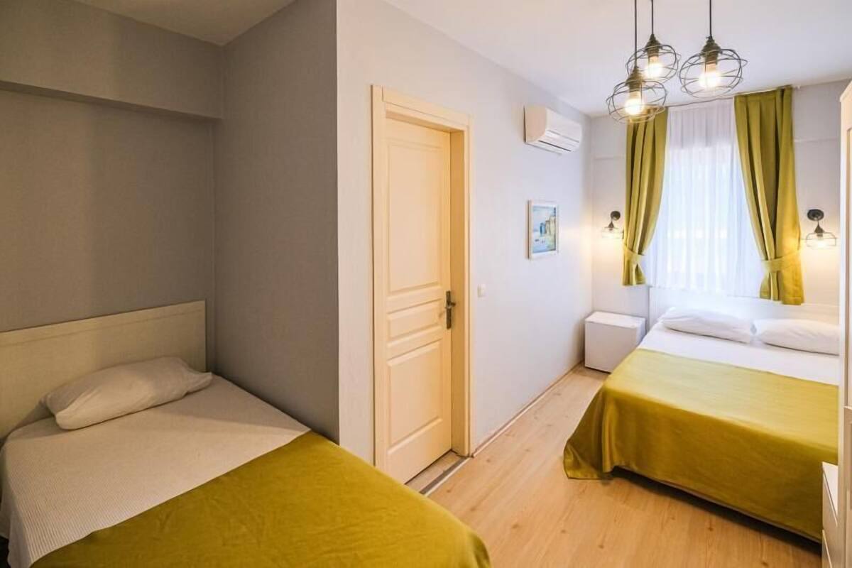 A hotel room with two beds, a door, a window with curtains, and a wall-mounted air conditioner.