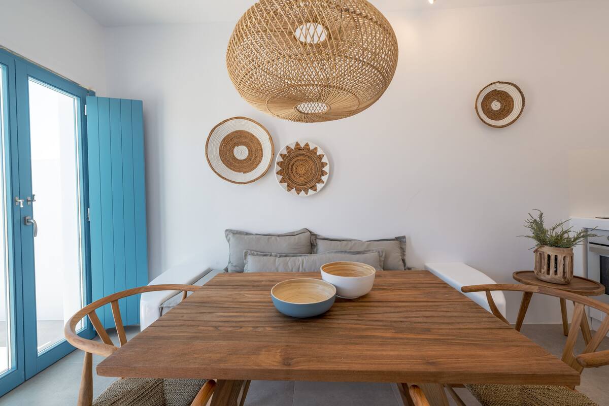 Un área de comedor con una mesa de madera, dos tazones, una lámpara colgante de fibras naturales y una puerta azul.