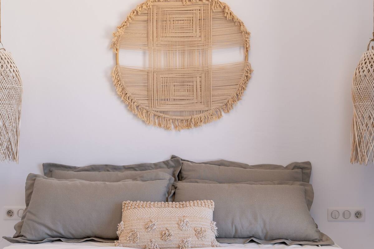 Una cama con ropa de cama gris y un tapiz circular tejido en la pared.