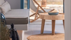 Un salon moderne avec un canapé, une table ronde en bois sur laquelle est posé un saladier, et une vue sur un paysage désertique par une porte ouverte.