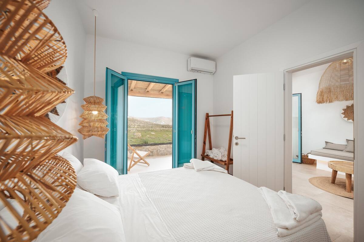 Un dormitorio con cama, una silla de mimbre y vistas al exterior.