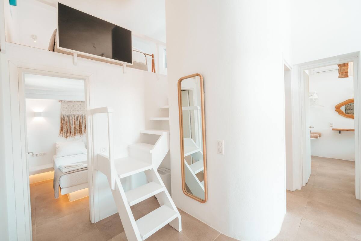 Un interior moderno y luminoso, con una escalera, un espejo grande y una cama con cabecera.