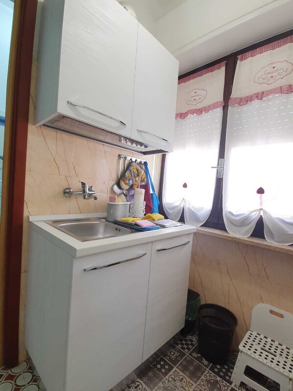 A compact kitchen with white cabinets, a sink, and a window with curtains.