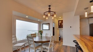 A dining area with a round wooden table, white chairs, and a chandelier. - Chic Port Angeles Home w/ Oceanfront Balcony! (Port Angeles)