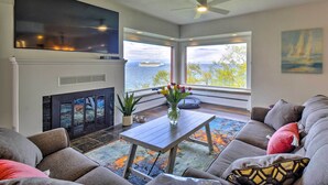 A living room with a fireplace, a sofa, a coffee table, and a view of the ocean. - Chic Port Angeles Home w/ Oceanfront Balcony! (Port Angeles)
