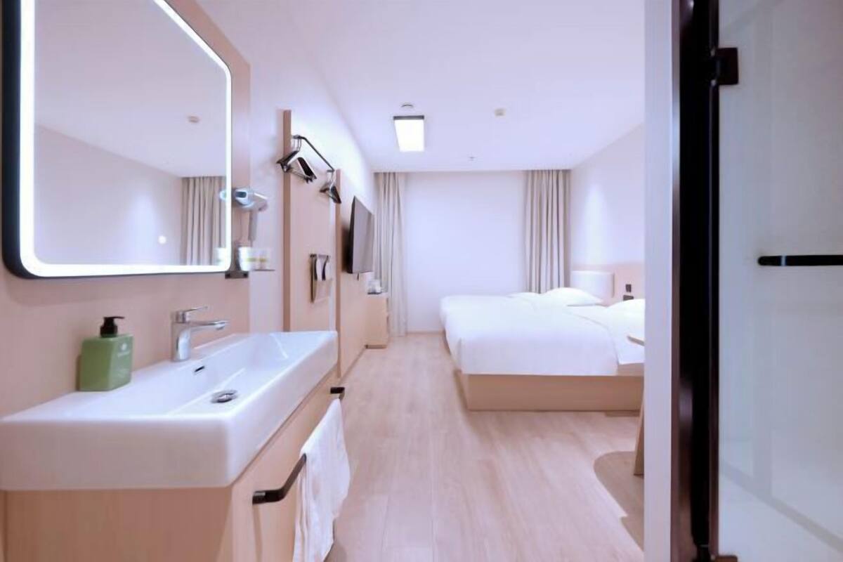 Habitación de hotel con un espejo grande, un lavamanos, una cama y un televisor.