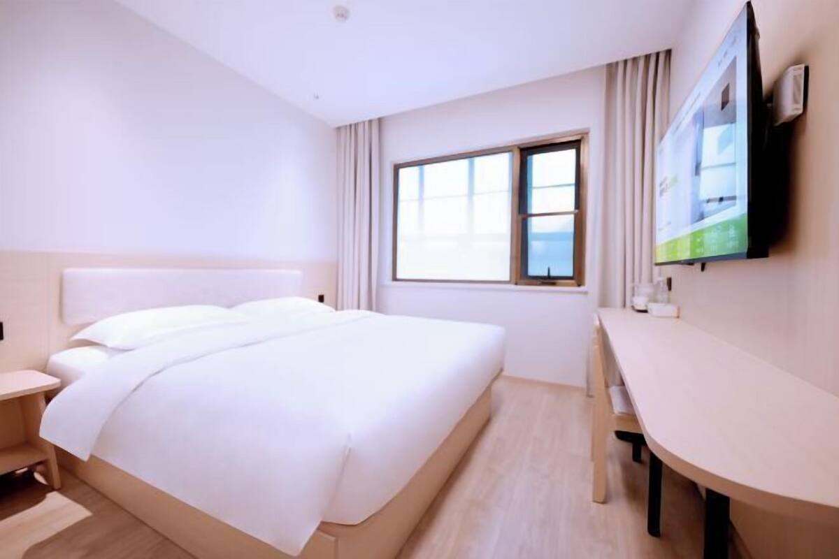 Habitación de hotel con cama, escritorio, silla, televisor y ventana.
