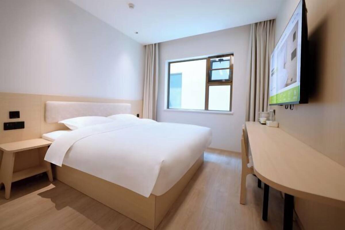 Habitación de hotel con cama, mesita de noche, escritorio y televisor instalado en la pared.