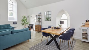 A modern living room with a teal sofa, a wooden dining table with blue chairs, and a patterned rug. - No 5 Old Church (Ventnor)