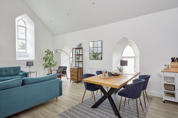 A modern living room with a teal sofa, a wooden dining table with blue chairs, and a patterned rug.