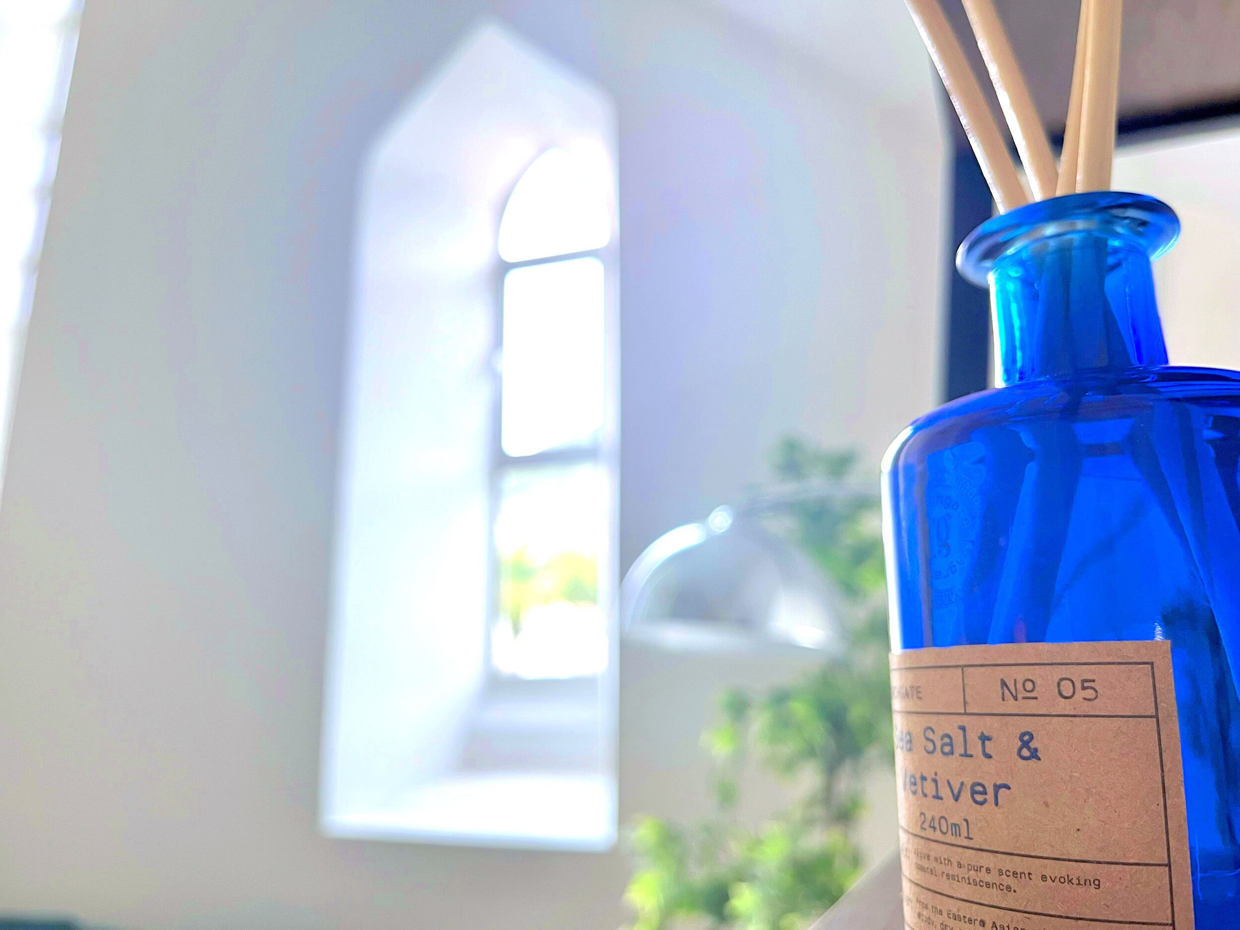 A blue bottle labeled 'Salt & River' with a volume of 240ml, placed in a room with a window and a plant in the background.