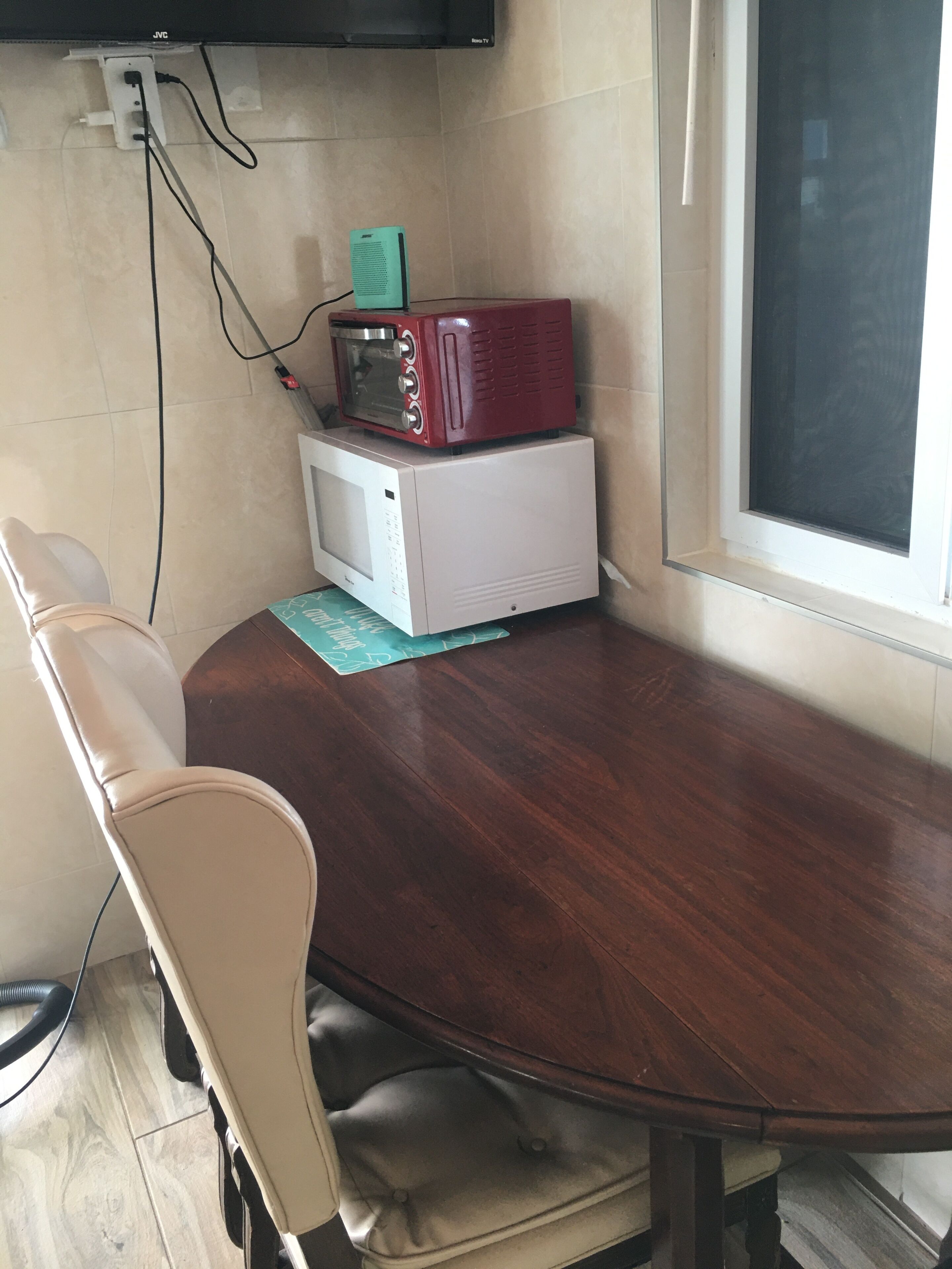 A dining area with a wooden table, two chairs, a microwave, and a red appliance on top.