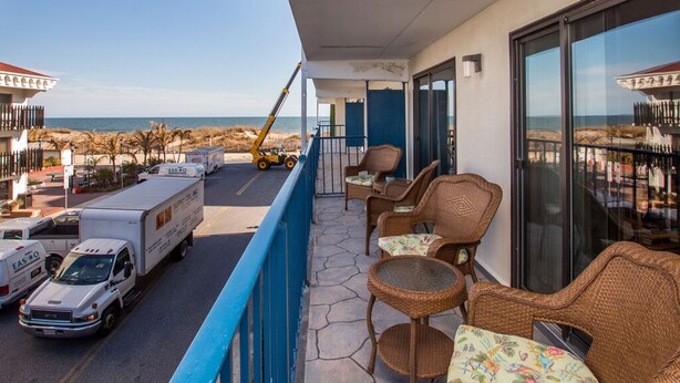 Un balcón con mobiliario de mimbre, vista a la playa y camiones estacionados.