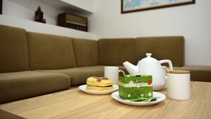 A cozy living room with a brown sofa, a wooden coffee table, a white teapot, a white mug, and a green box of tea. - Furnas Sweet Home - Central Zone (Furnas)