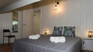 A bedroom with a large bed, two bedside lamps, a chair, and a door leading to a bathroom. - Furnas Sweet Home - Central Zone (Furnas)