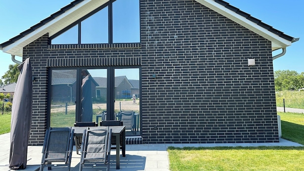Een modern gebouw met een ruime glazen ingang, terrasplekken en een gevel van baksteen.