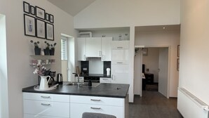 Een moderne keuken met witte kastjes, een zwart aanrecht en een grijze stoel. Er hangen ingelijste foto's aan de muur en staat een plant in een pot op het aanrecht.