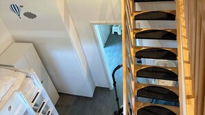 Een houten trap met een leuning die leidt naar een verdieping erboven. Een stofzuiger is zichtbaar op de verdieping beneden.