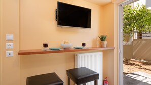 A kitchen with a TV mounted above a wooden countertop, a white radiator below, and two black stools. - Athens Riviera Golf Apartment (Glyfada)
