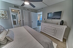 Ein Schlafzimmer mit Bett, Kommode, Fernseher und einem Flur zum Badezimmer.