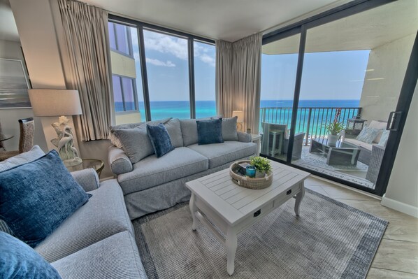 Ein modernes Wohnzimmer mit grauem Sofa, einem weißen Couchtisch und Meerblick durch große Fenster.