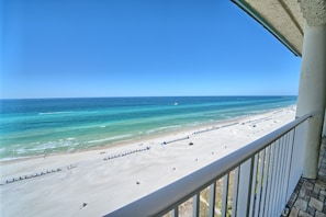 Blick auf einen Strand vom Balkon mit Geländer, klarer Himmel und ruhiges Meer.