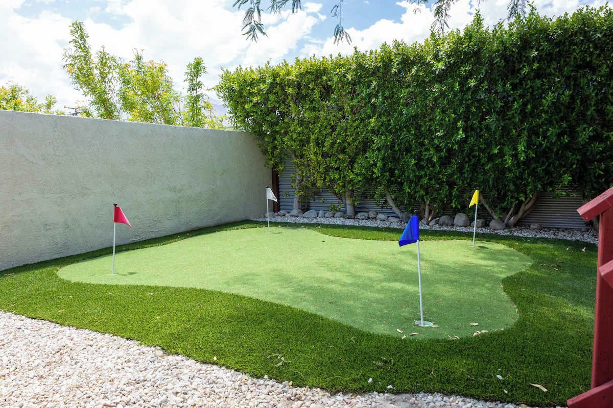 A well-maintained artificial grass area with three flags, surrounded by a low stone wall and a dense hedge.