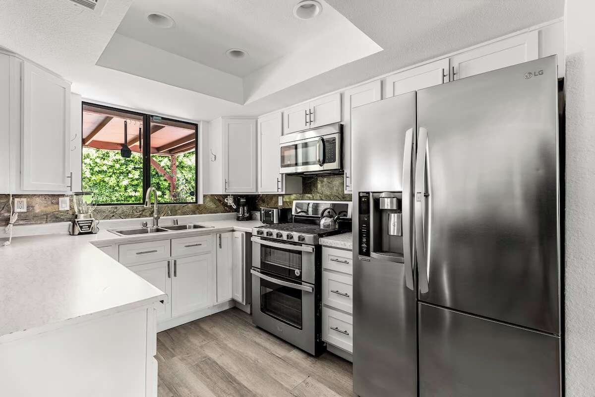 Bright kitchen with white shaker cabinets, quartz counters, double oven, and garden window — fully equipped for a group breakfast after a late pool night