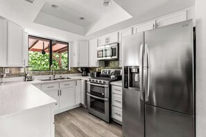 Bright kitchen with white shaker cabinets, quartz counters, double oven, and garden window — fully equipped for a group breakfast after a late pool night
