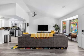 A modern living space with a grey sofa, a flat-screen TV, and a kitchen area with stainless steel appliances.