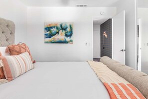 A hotel room with a large bed, a painting on the wall, and a view of the hallway.