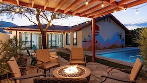 A covered outdoor patio with wicker furniture, a fire pit, and a pool.