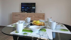 Un comedor con mesa de vidrio, cuencos blancos y un televisor al fondo.